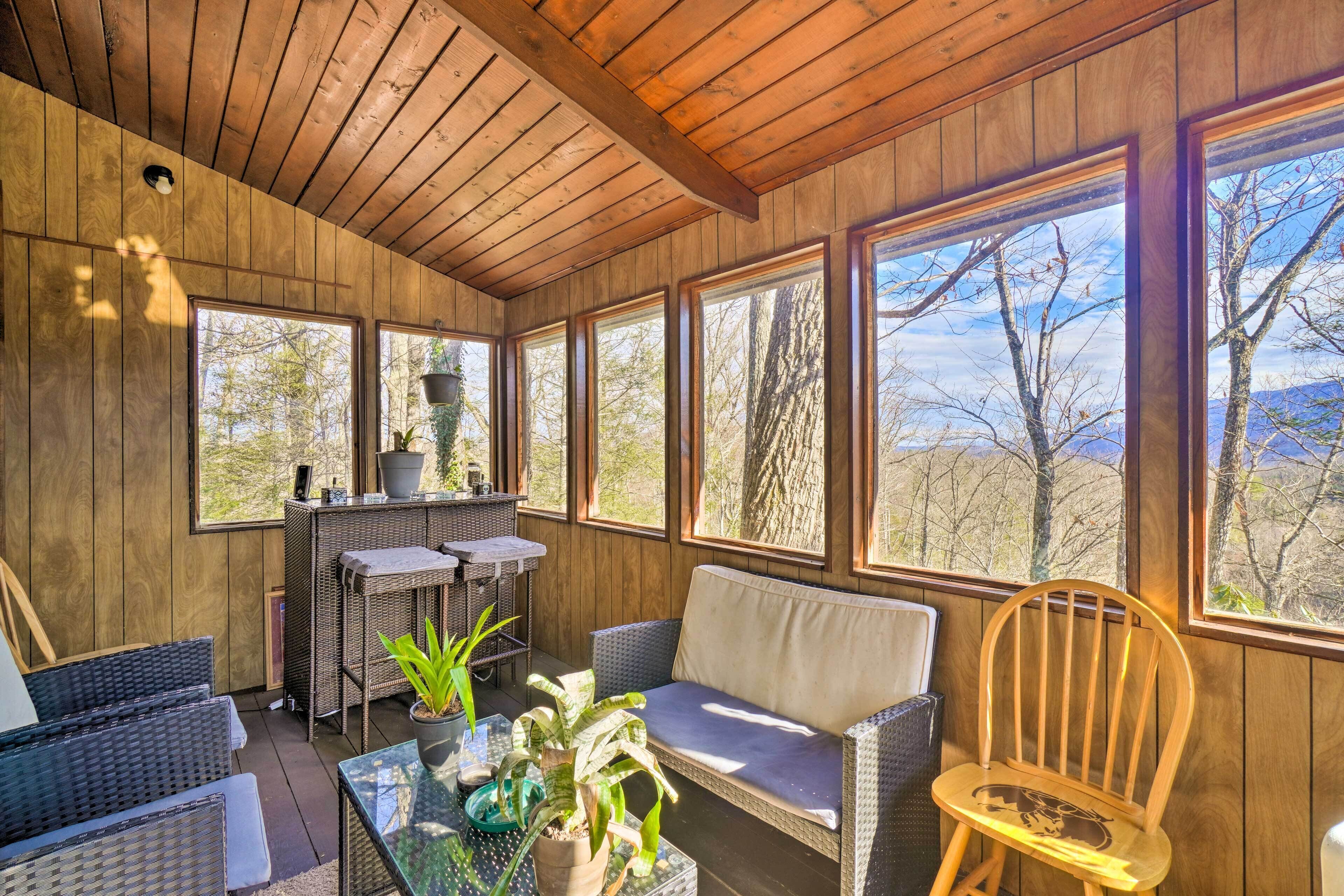 Ein Zimmer mit Holzwänden, Korbmöbeln, großen Fenstern und Blick auf Bäume.