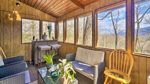 Una habitación con paneles de madera, muebles de mimbre, ventanas amplias y vistas a árboles.