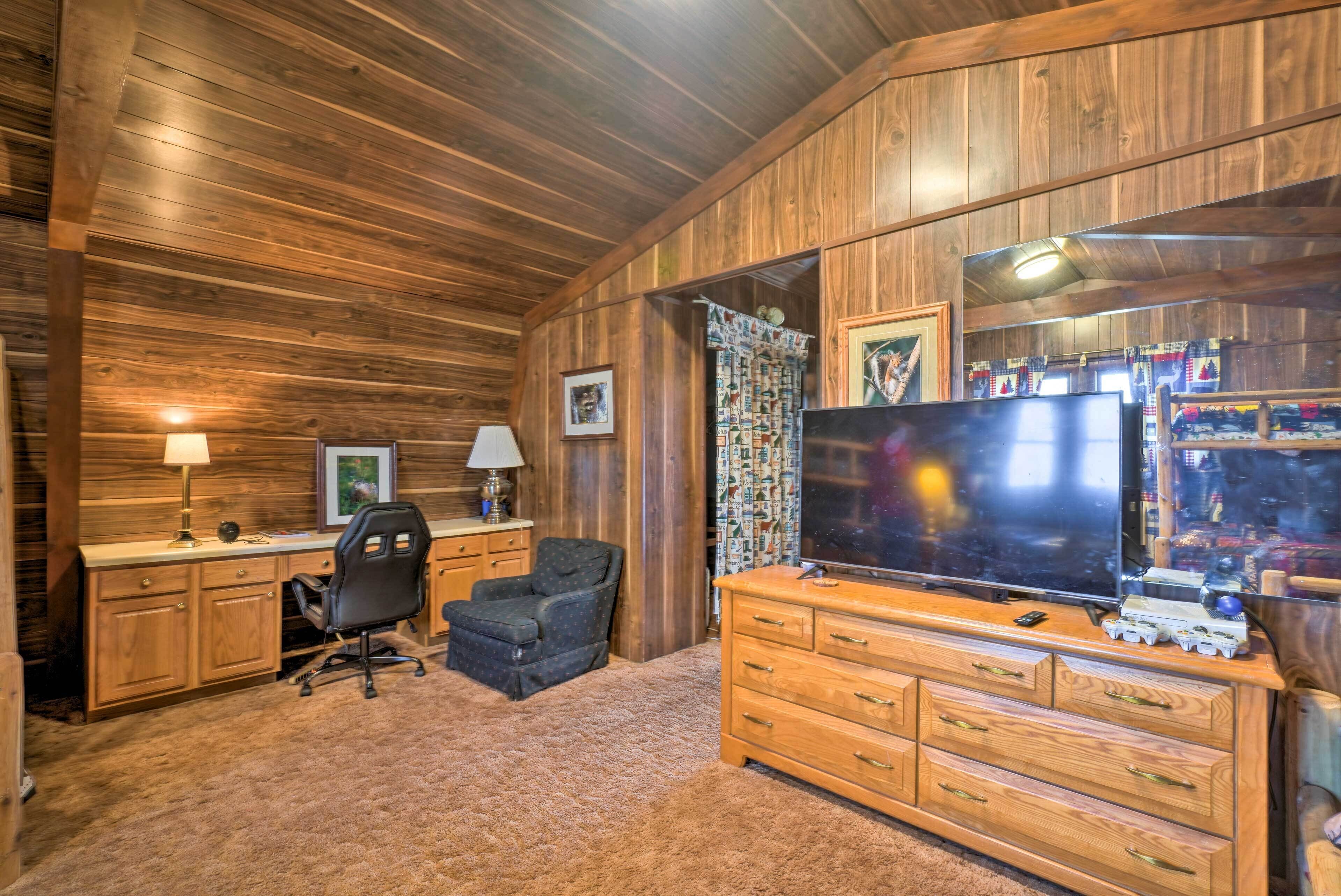 A cozy room with wooden walls and ceiling, a large flat-screen TV, a wooden dresser, a desk with a chair, and a carpeted floor.