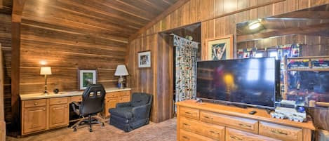 A cozy room with wooden walls and ceiling, a large flat-screen TV, a wooden dresser, a desk with a chair, and a carpeted floor.