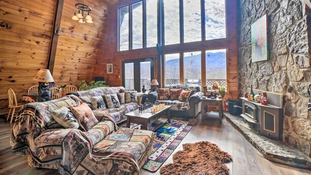 Interior acogedor de una cabaña de madera con techo de madera, pared de piedra, chimenea y un ventanal con vistas a la montaña.