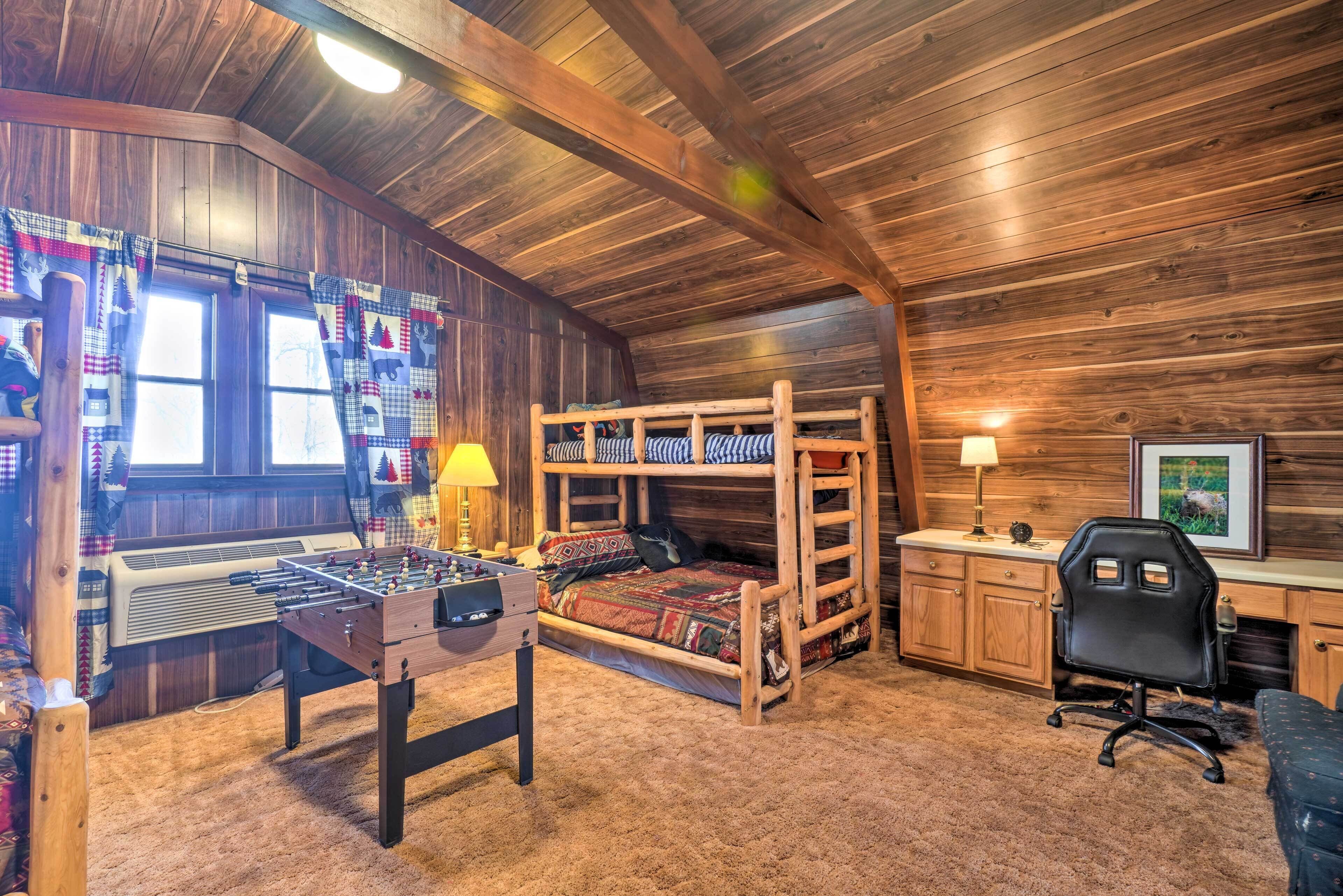 A cozy room with a wooden ceiling, a bunk bed, a foosball table, a desk with a chair, and a window with curtains.