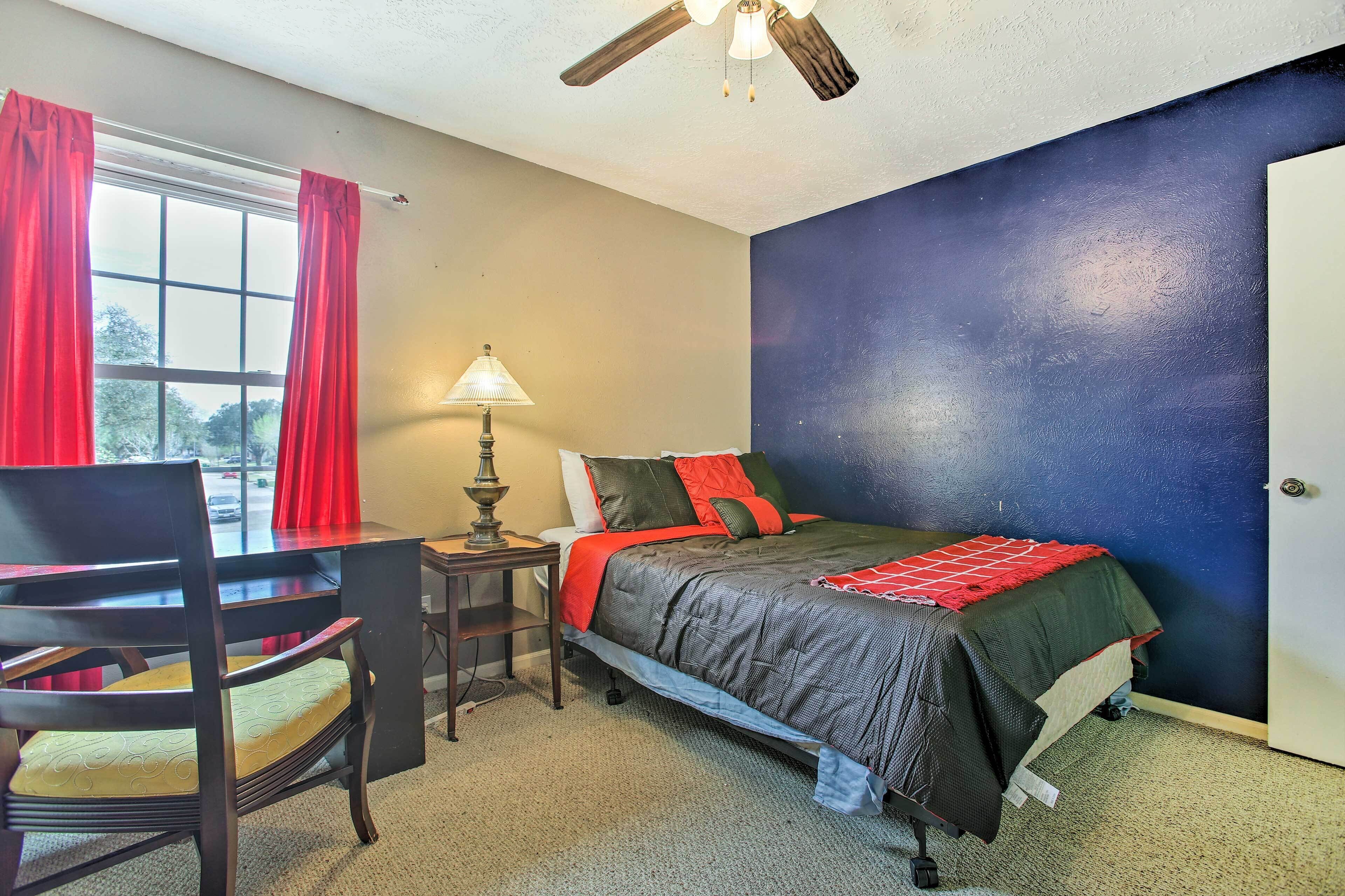 A bedroom with a bed, a desk, a chair, a lamp, and a window with curtains.
