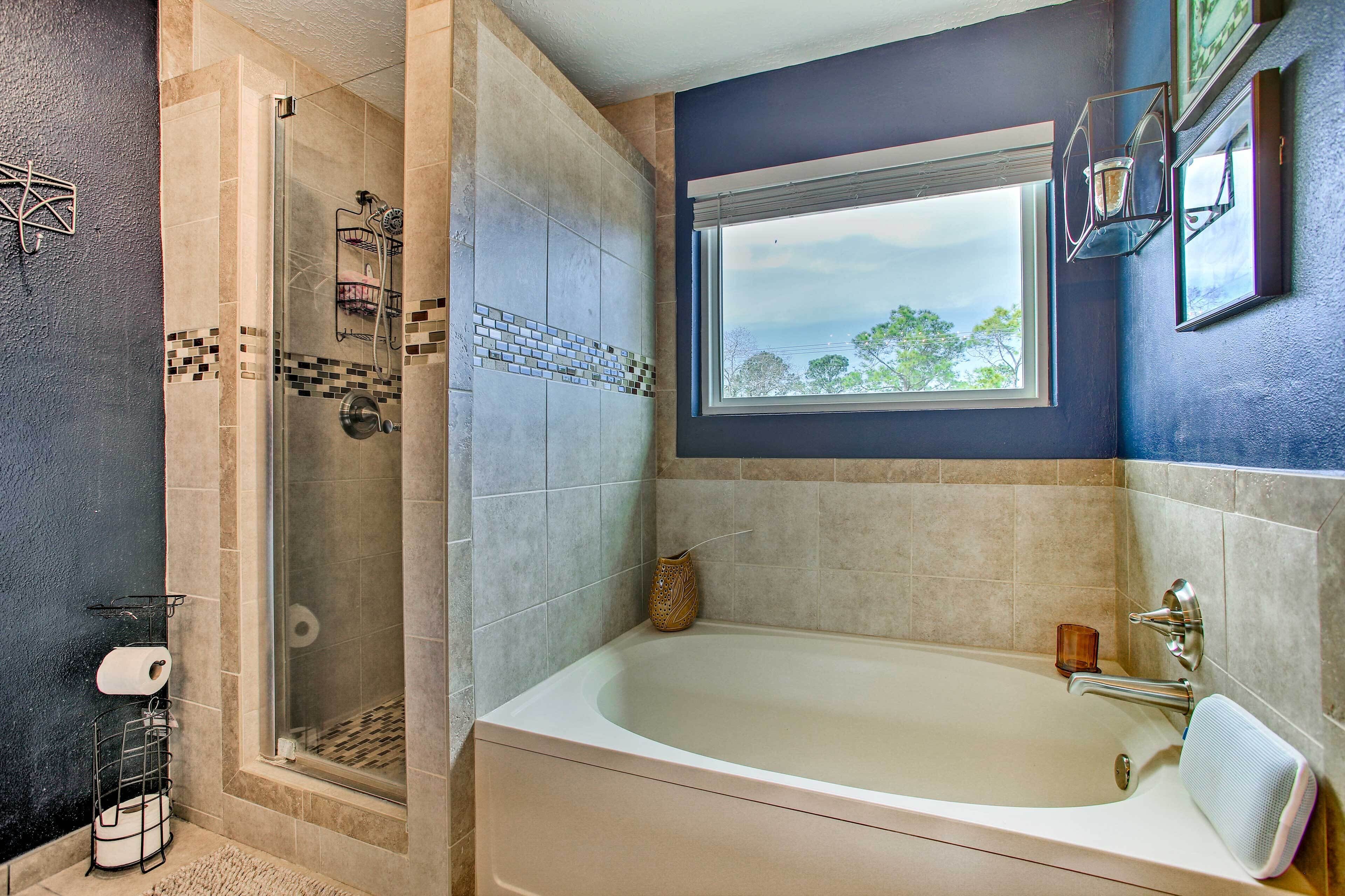 Un bagno moderno con doccia vetrata, una vasca e una finestra con vista sugli alberi.