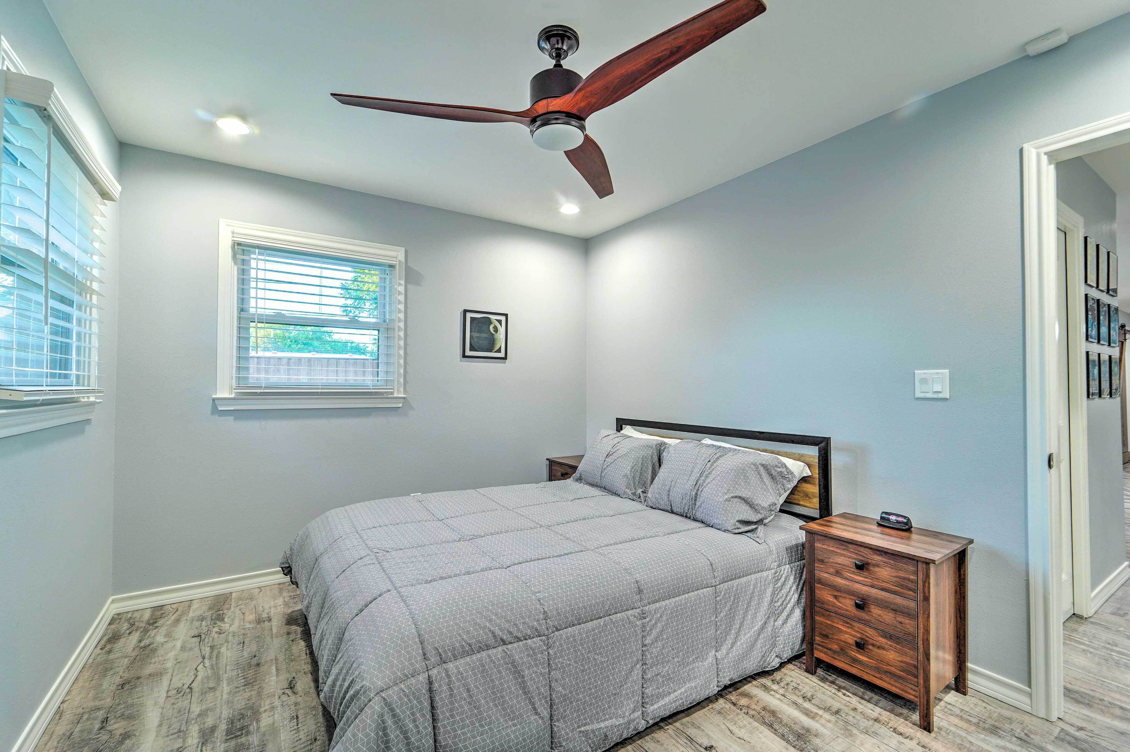 A bedroom with a bed, nightstand, ceiling fan, window, and a framed picture on the wall.