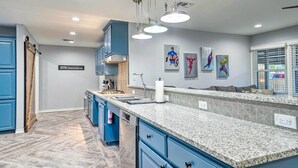 Een moderne keuken met blauwe kastjes, granieten aanrecht en hangende lampen.