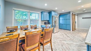Een moderne keuken met blauwe kastjes, een roestvrijstalen koelkast en een eethoek met houten stoelen en een tafel.