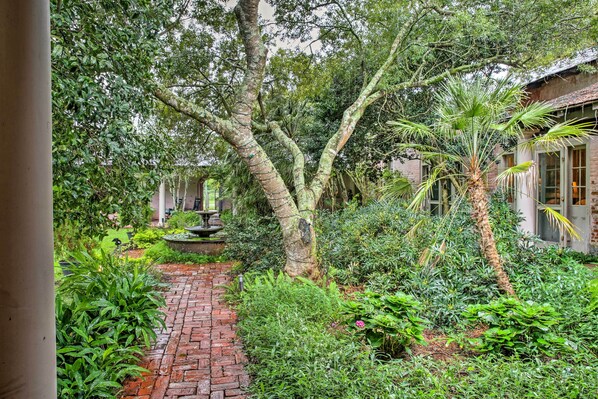 A lush garden with a brick pathway, a large tree, and a building with windows. - Historic Baton Rouge Vacation Rental: 6 Mi to Lsu! (Baton Rouge)