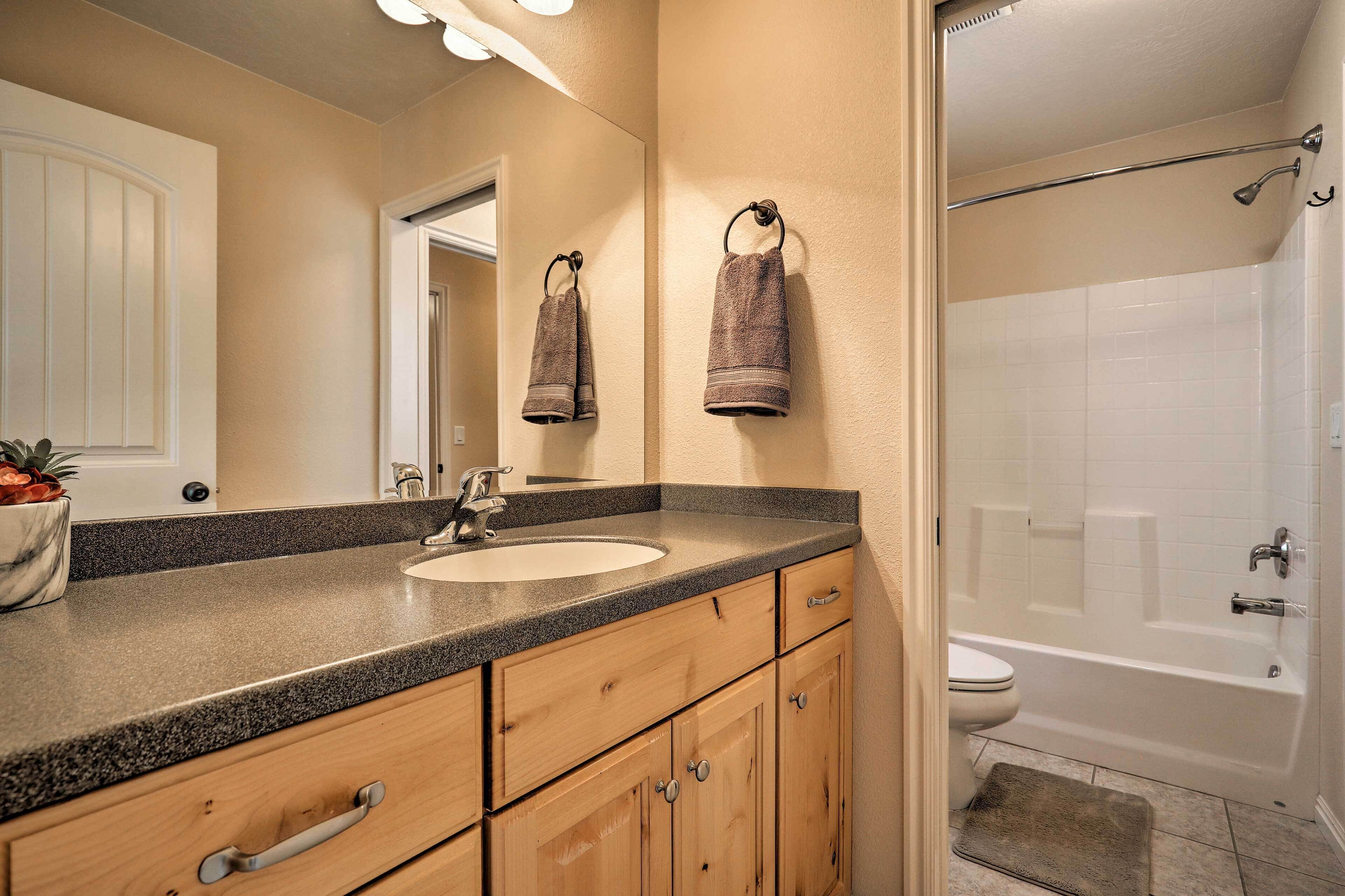 A bathroom with a sink, mirror, towel rack, wooden cabinets, and a bathtub.