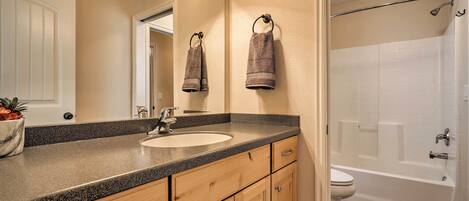 A bathroom with a sink, mirror, towel rack, wooden cabinets, and a bathtub.