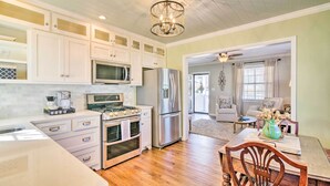 A kitchen with white cabinets, stainless steel appliances, and a wooden dining table. - Mississippi Cottage ~ 6 Mi to Columbus Lake (Columbus)