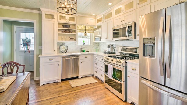 A kitchen with white cabinets, stainless steel appliances, a wooden dining table, and a chandelier. - Mississippi Cottage ~ 6 Mi to Columbus Lake (Columbus)