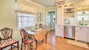 A dining area with a wooden table and chairs, a window with blinds, and a kitchen with white cabinets and a dishwasher. - Mississippi Cottage ~ 6 Mi to Columbus Lake (Columbus)