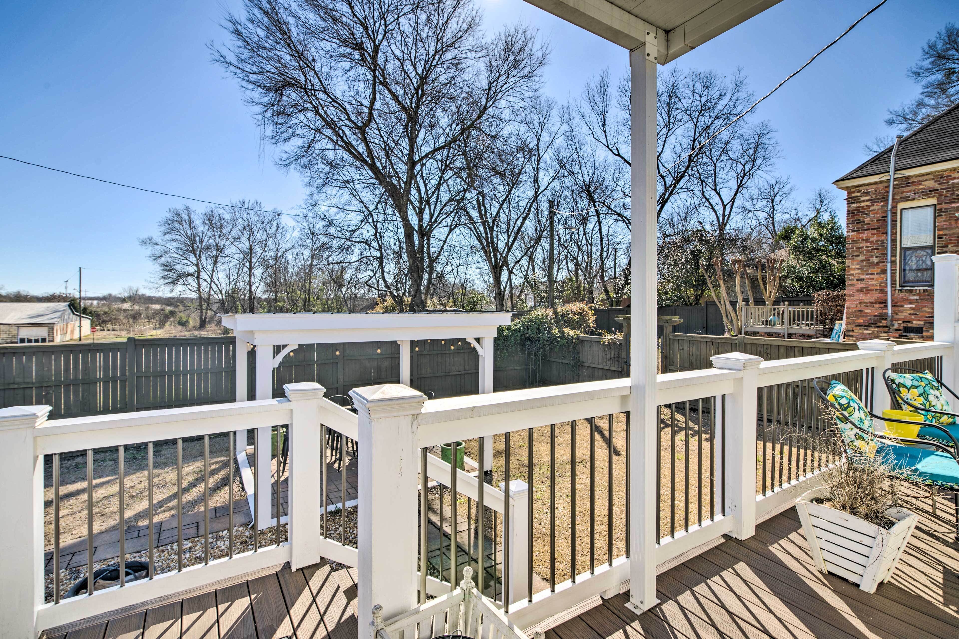 Une terrasse en bois avec des rampes blanches, un patio couvert et une maison en briques en arrière-plan.