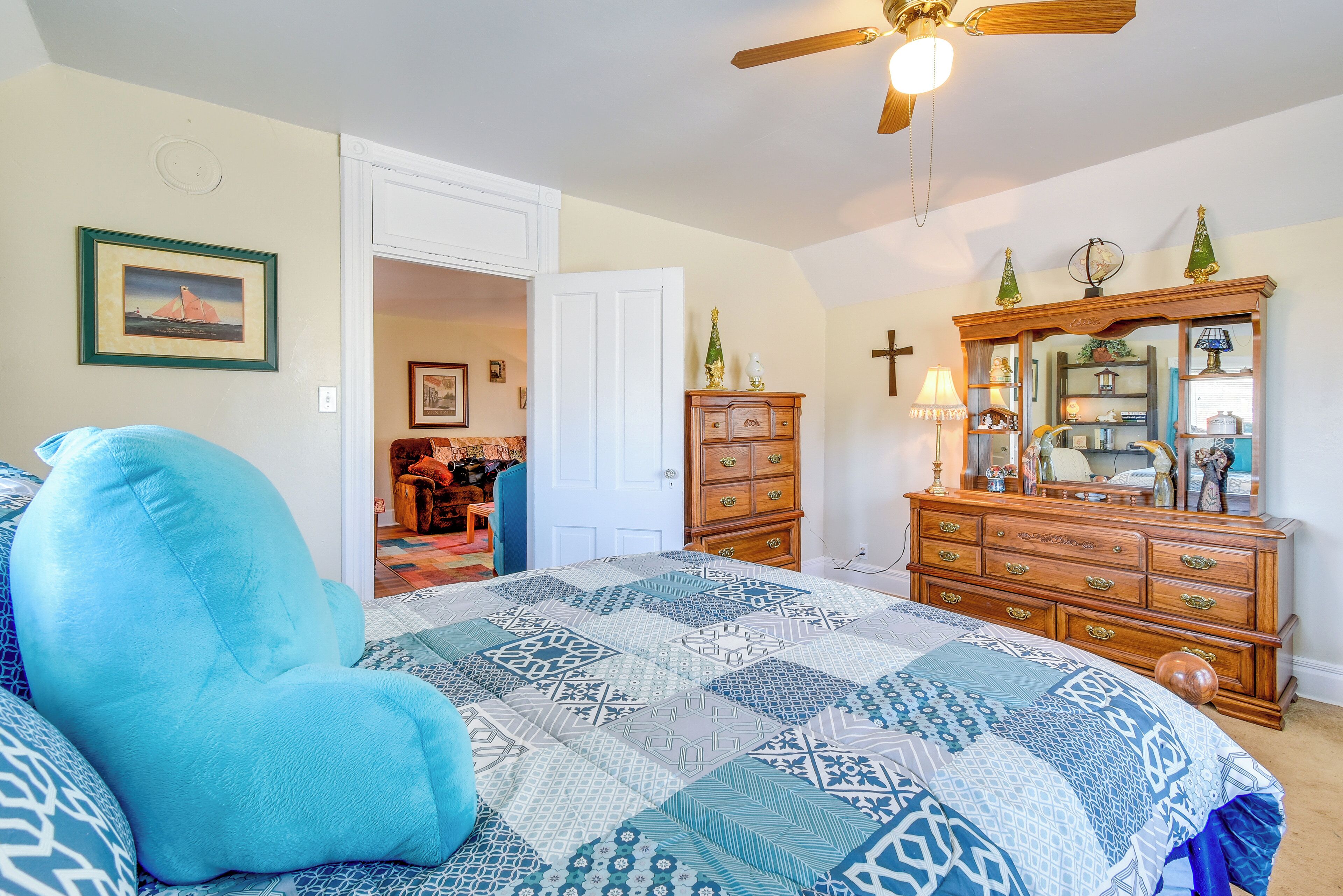 A bedroom with a large bed, a wooden dresser, a mirror, and a ceiling fan.