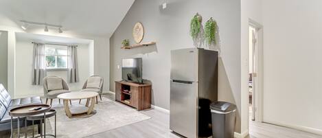 A modern living room with a sofa, two armchairs, a coffee table, a TV, a refrigerator, and a trash bin.