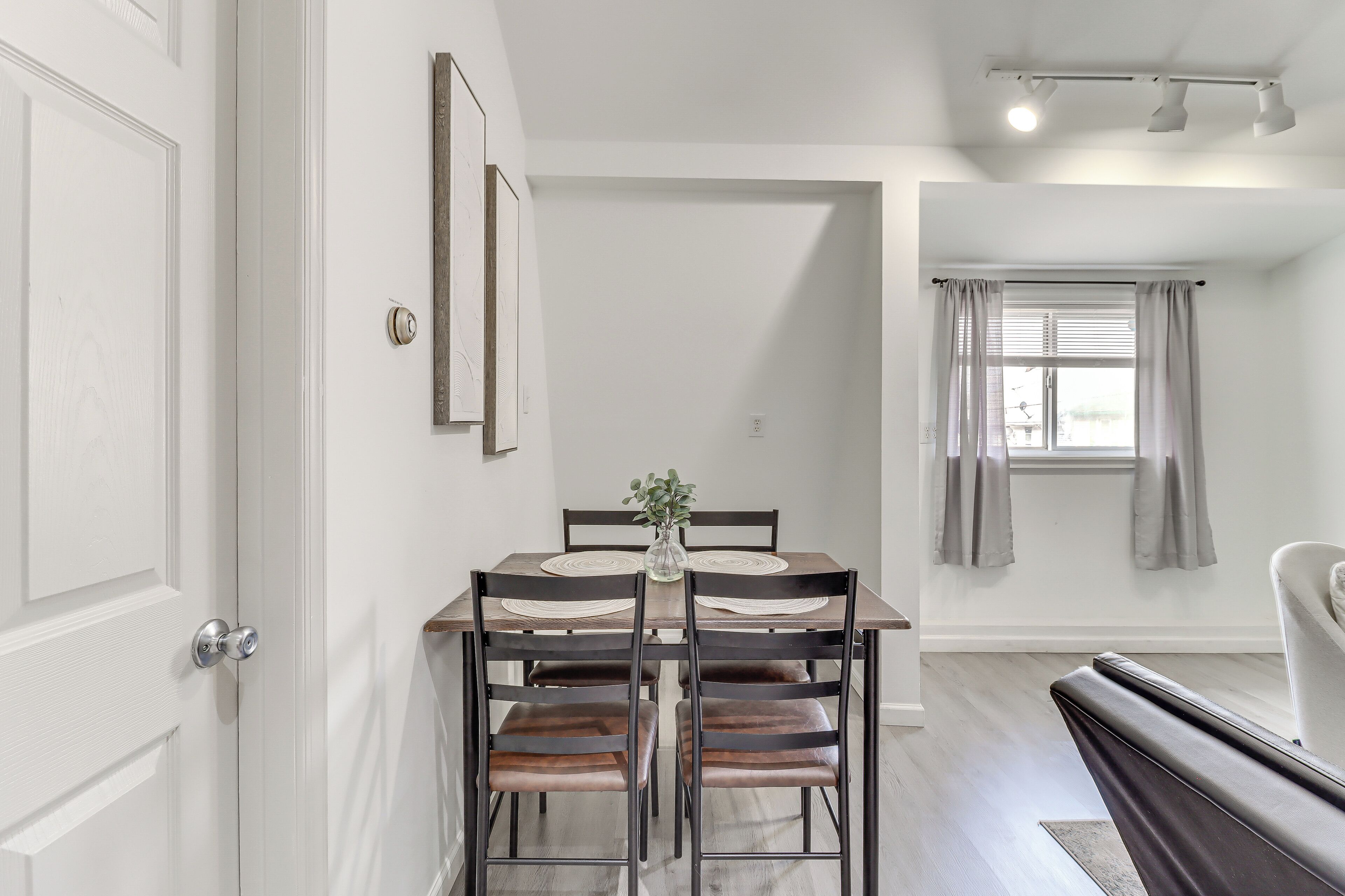 A dining area with a wooden table and four chairs, a vase with greenery, and a window with curtains.