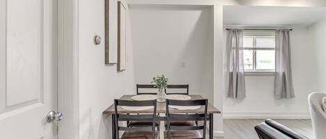 A dining area with a wooden table and four chairs, a vase with greenery, and a window with curtains.