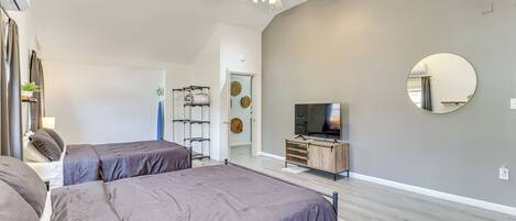 A modern bedroom with two beds, a TV, and a ceiling fan.