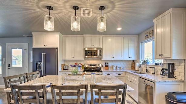 Una cocina moderna con armarios blancos, encimera de granito y una isla central con sillas de madera.