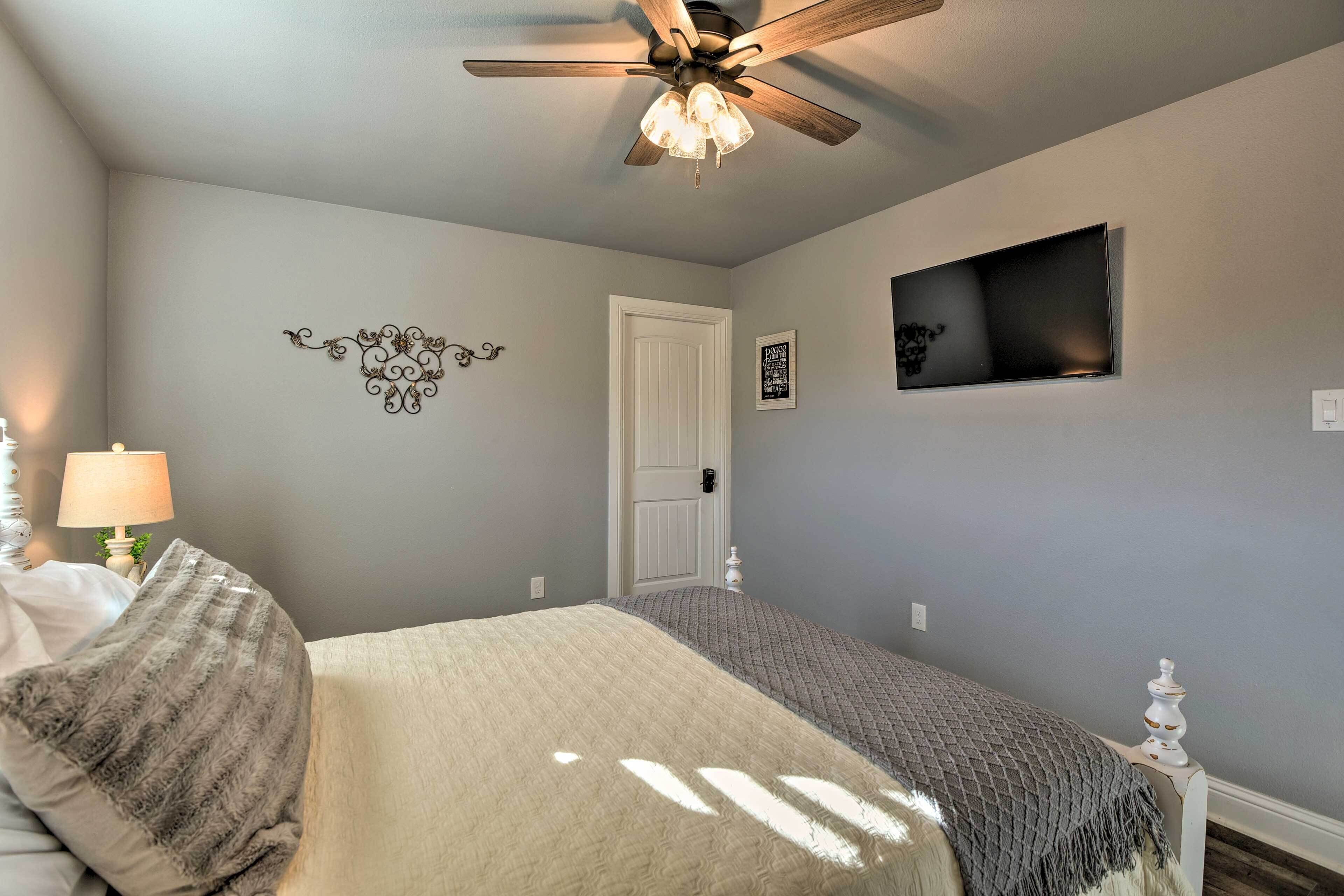 Une chambre à coucher avec un lit, un ventilateur de plafond, une télévision et une porte.