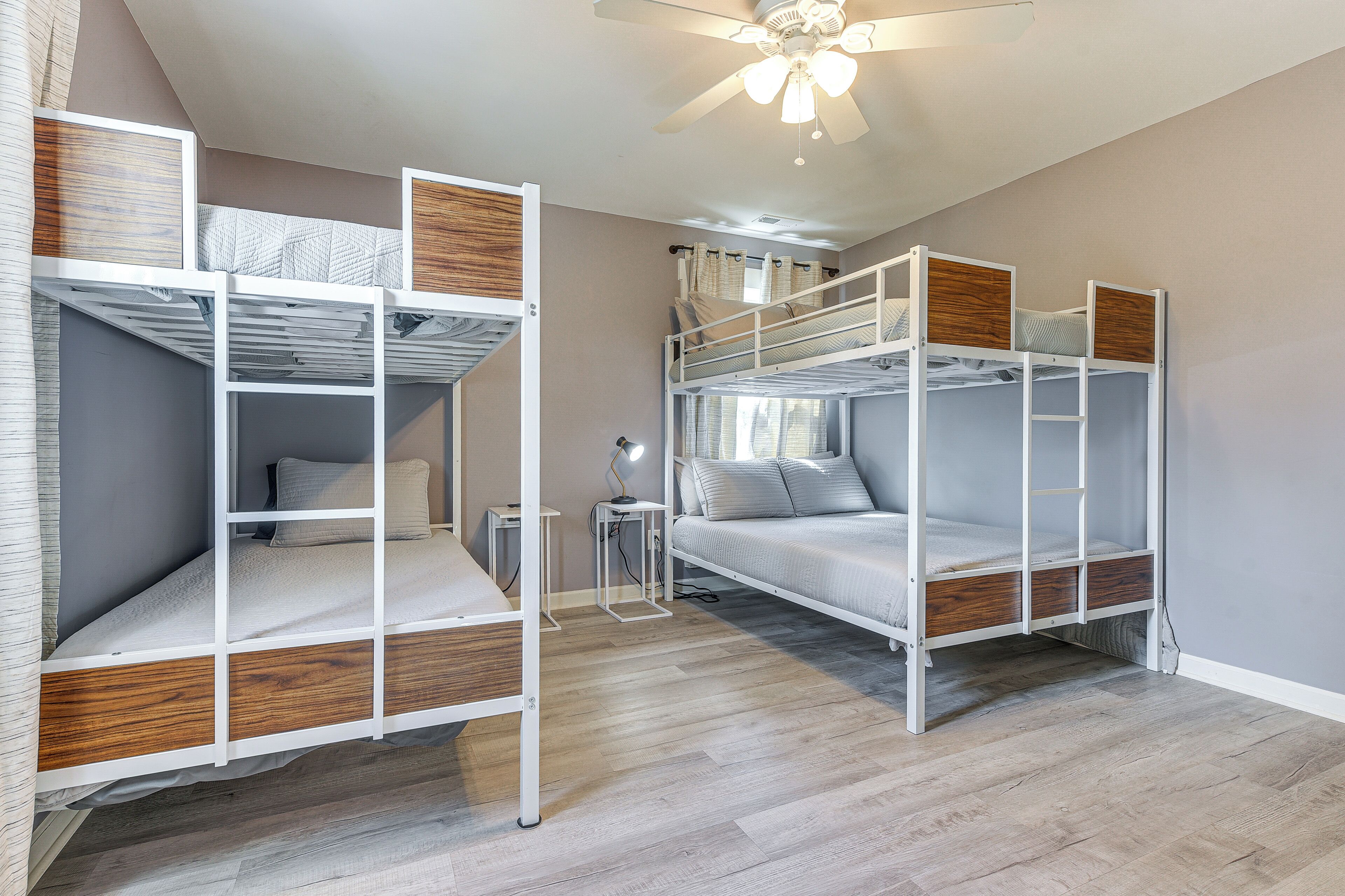 A room with bunk beds, a ceiling fan, and a small table with a lamp.