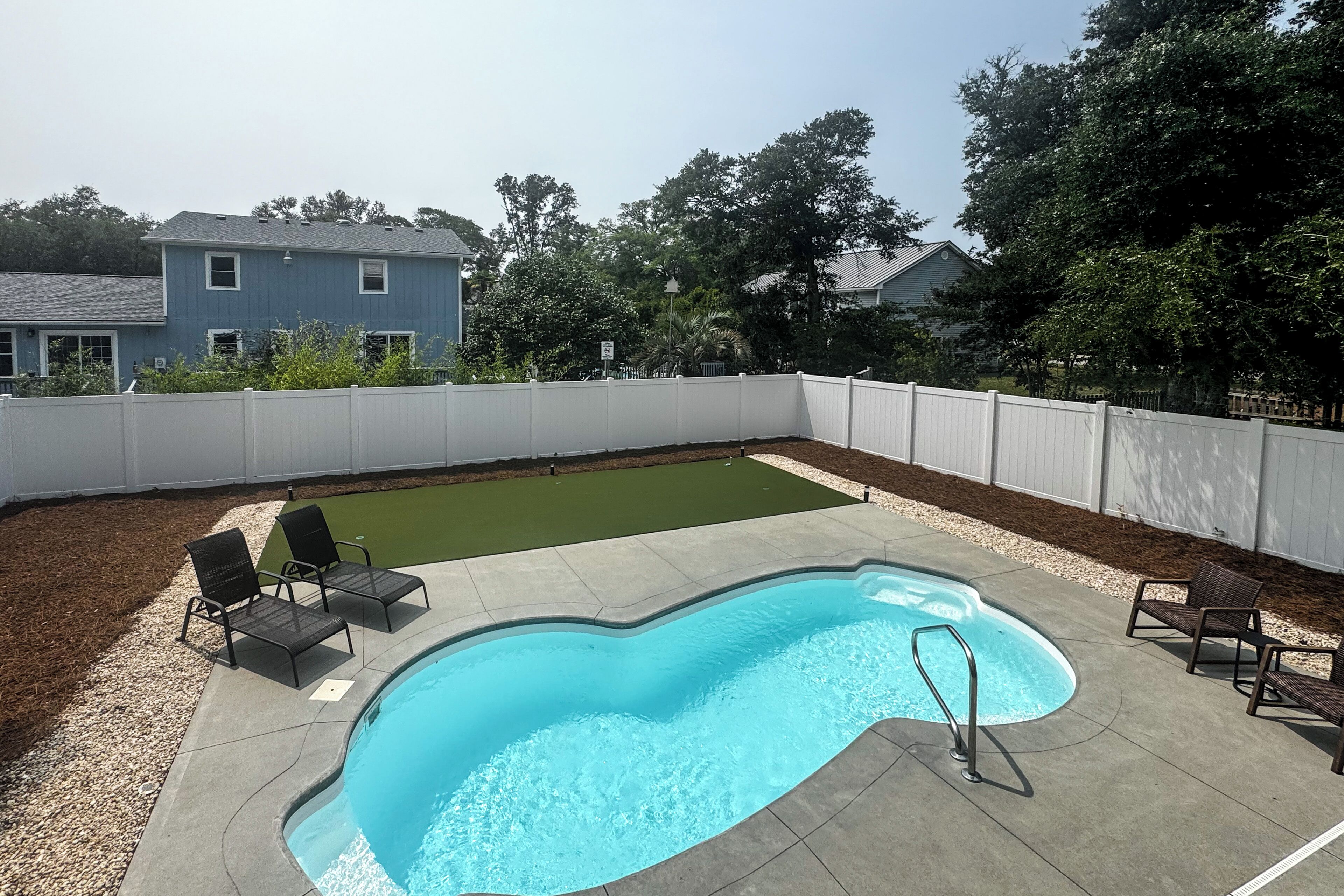 A backyard with a swimming pool, two lounge chairs, and a small lawn area.