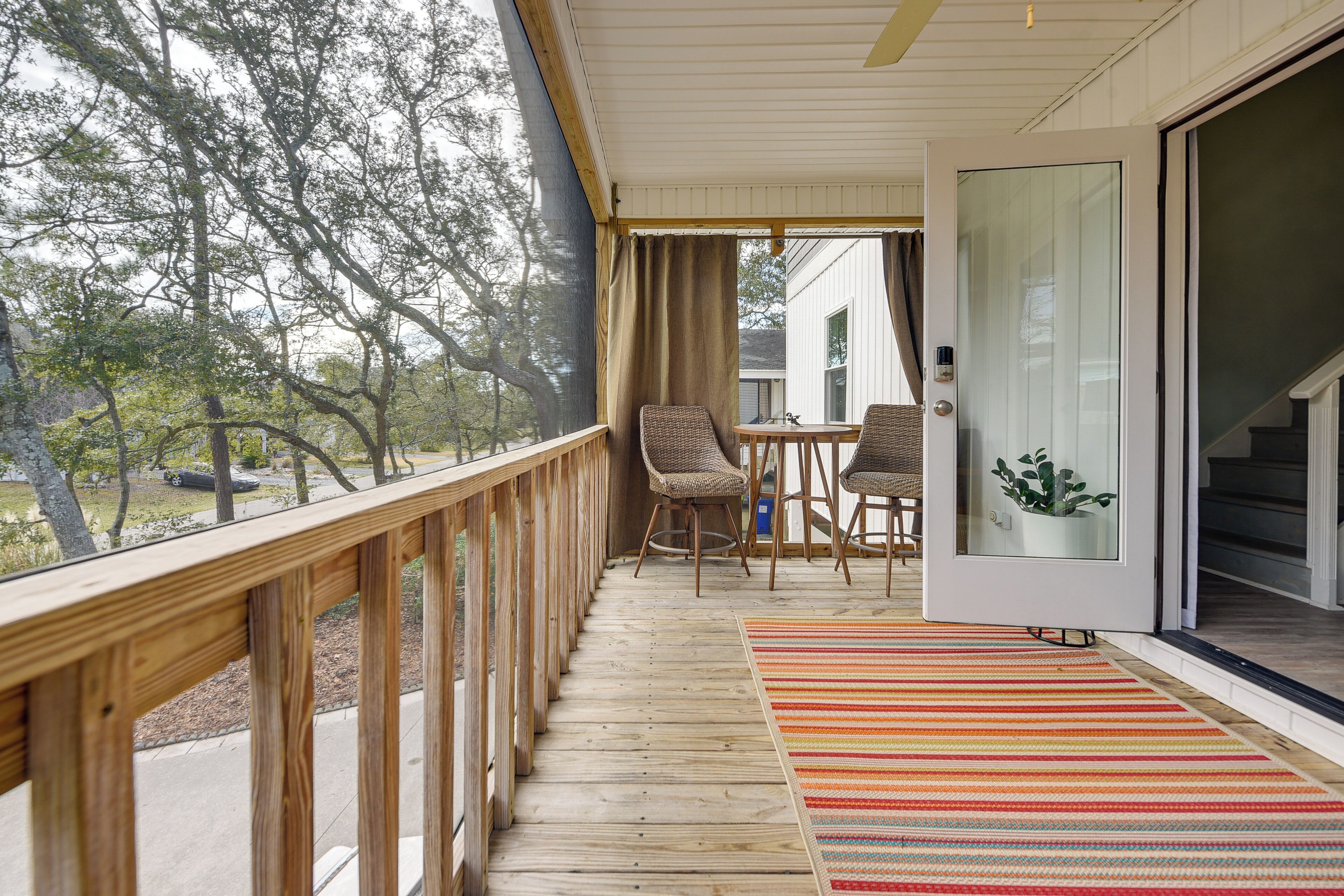 A wooden deck with wicker chairs and a table, a sliding glass door, and a view of trees.