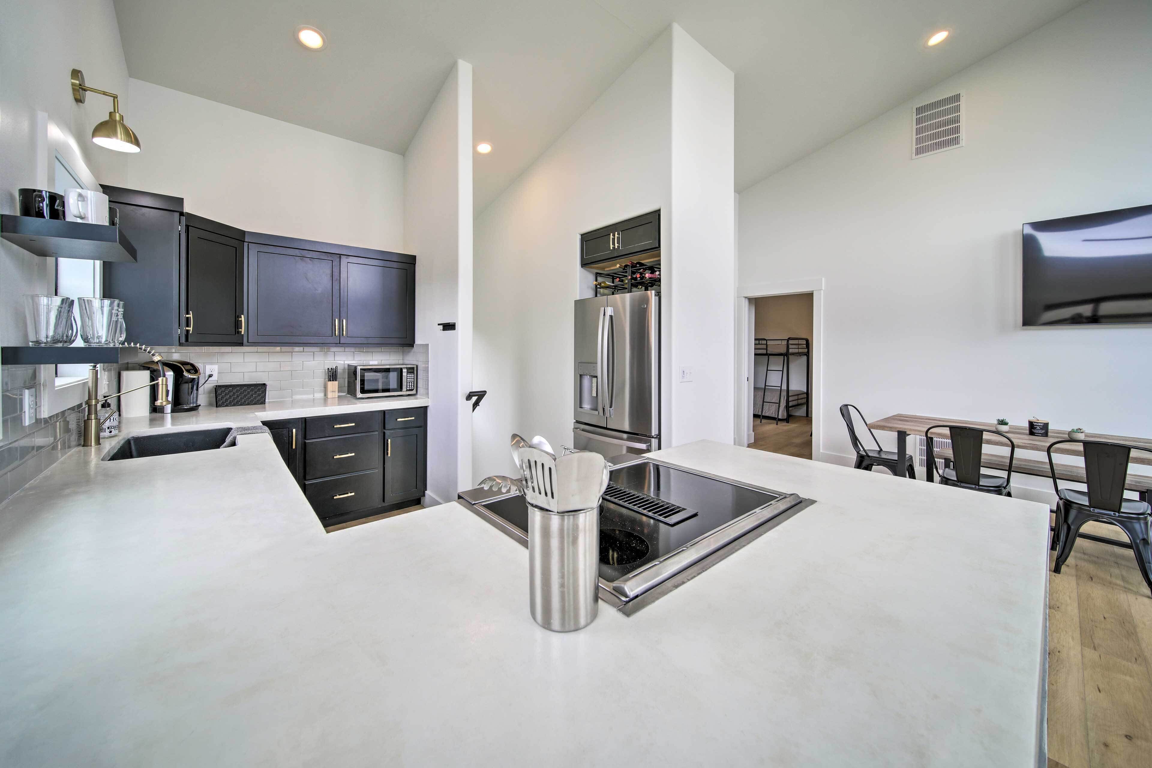 A modern kitchen with dark cabinets, stainless steel appliances, and a central island with a sink and utensils.