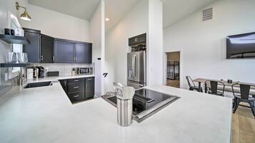 A modern kitchen with dark cabinets, stainless steel appliances, and a central island with a sink and utensils.