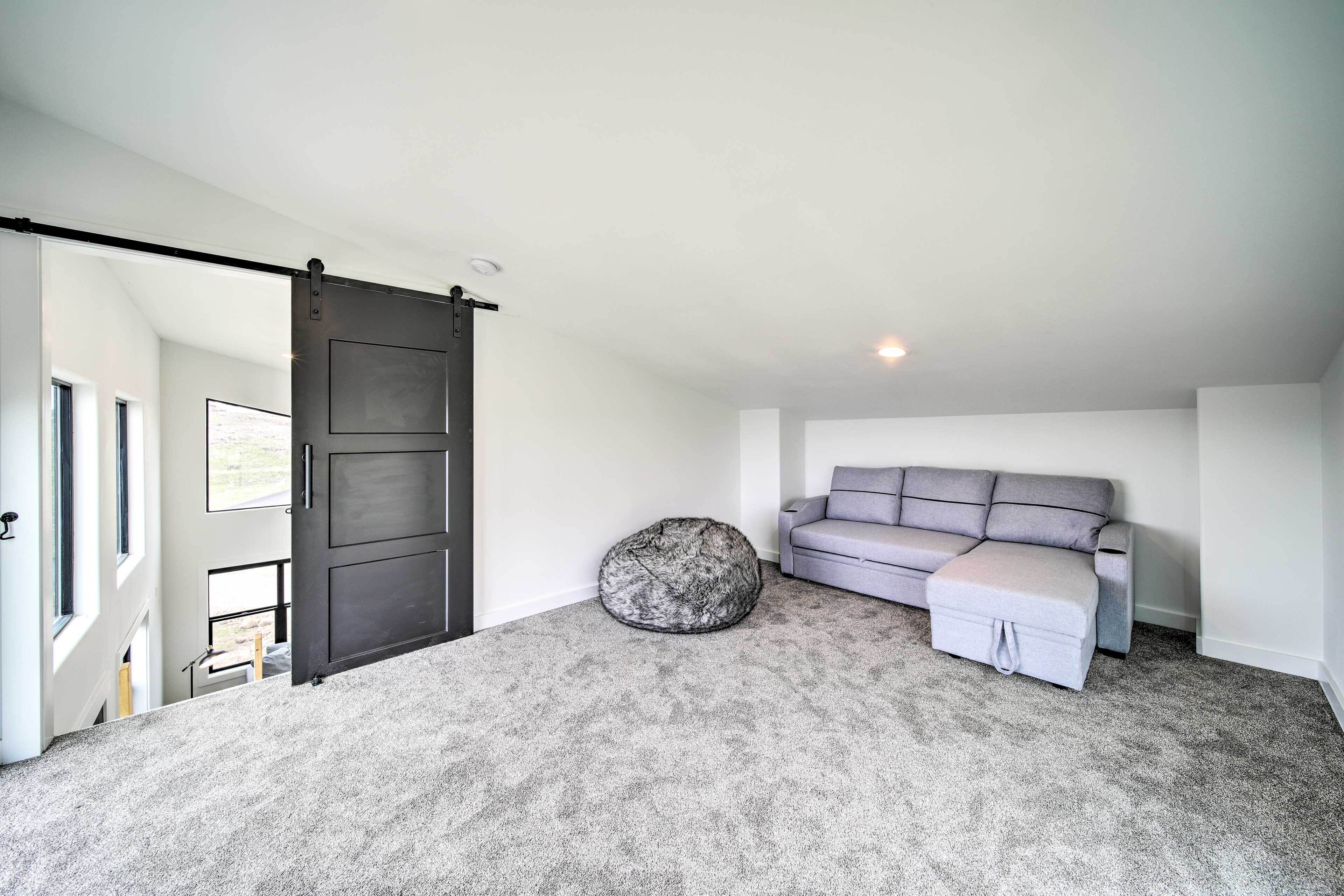 A modern living room with a grey sofa, a bean bag, and a sliding door.