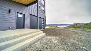 A modern building with a grey exterior, a wooden overhang, and a gravel driveway leading to a set of concrete steps. - Modern Davenport Home w/ Water View & Grill! (Davenport)