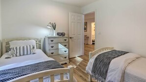 Een slaapkamer met twee bedden, een dressoir en een deur naar een andere kamer.