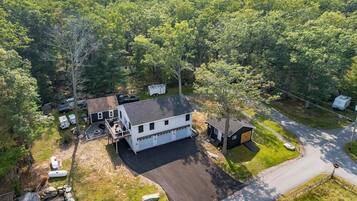A two-story house with a garage, surrounded by a wooded area.
