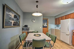 A compact kitchen with a dining table, chairs, a microwave, a refrigerator, and a painting on the wall.