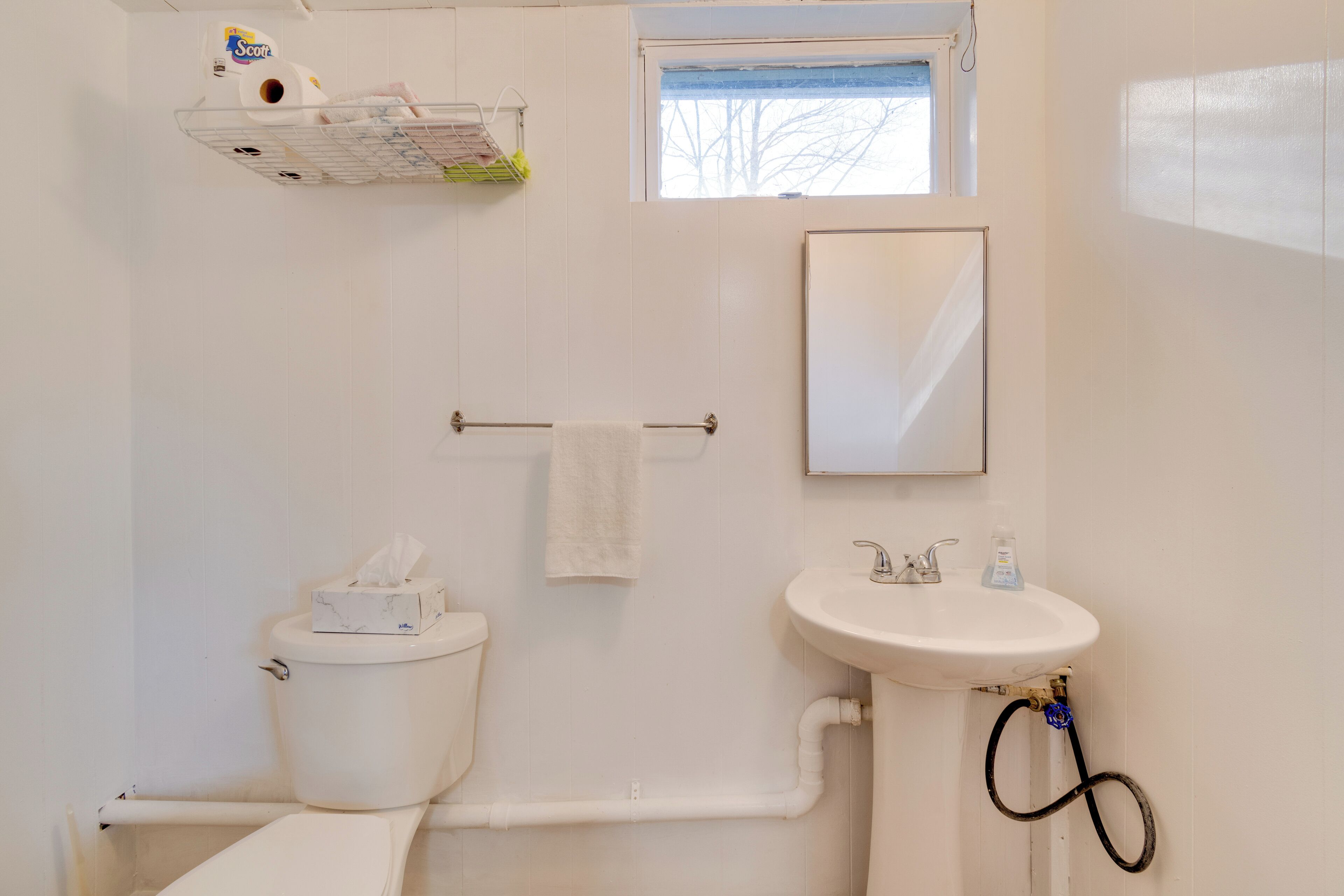 A bathroom with a toilet, sink, towel rack, and a small window.