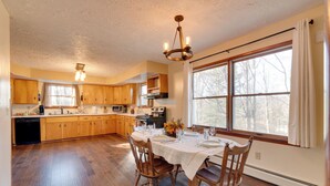 A spacious kitchen with wooden cabinets, a dining table set for four, and a large window providing a view of trees. - Peaceful Horseheads Hideaway w/ Deck & Yard! (Horseheads)
