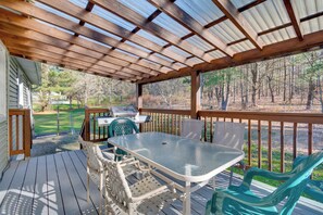 Une terrasse extérieure couverte, équipée d’une table et de chaises, d’un barbecue et offrant une vue sur une zone boisée.