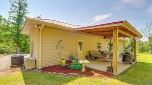 Une maison de plain-pied dotée d’un porche couvert, d’un patio aménagé avec du mobilier d’extérieur et d’un petit jardin avec des plantes et un abreuvoir pour les oiseaux.