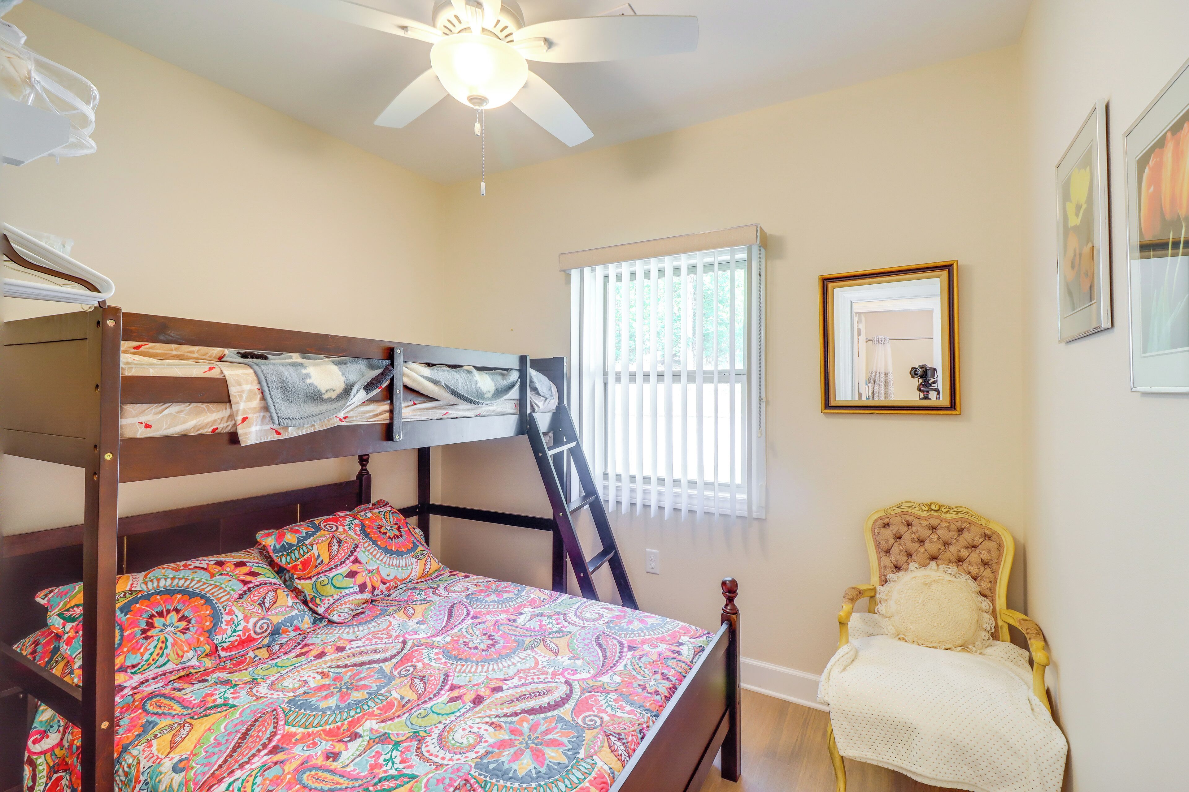 A bedroom with a bunk bed, a chair, a ceiling fan, and a window with blinds.