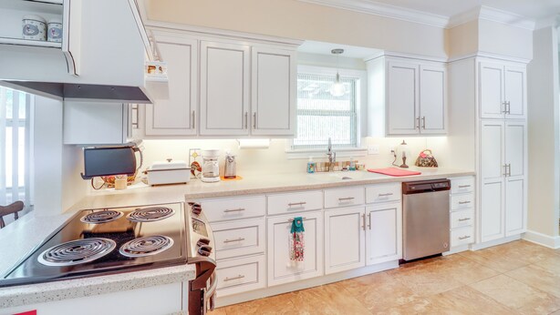Une cuisine moderne avec des meubles blancs, une cuisinière, un lave-vaisselle et une fenêtre qui laisse entrer la lumière naturelle.