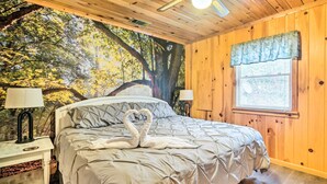 Een slaapkamer met een groot bed, twee bedlampen, een raam met uitzicht op bomen en een muurschildering van een bos op de muur.