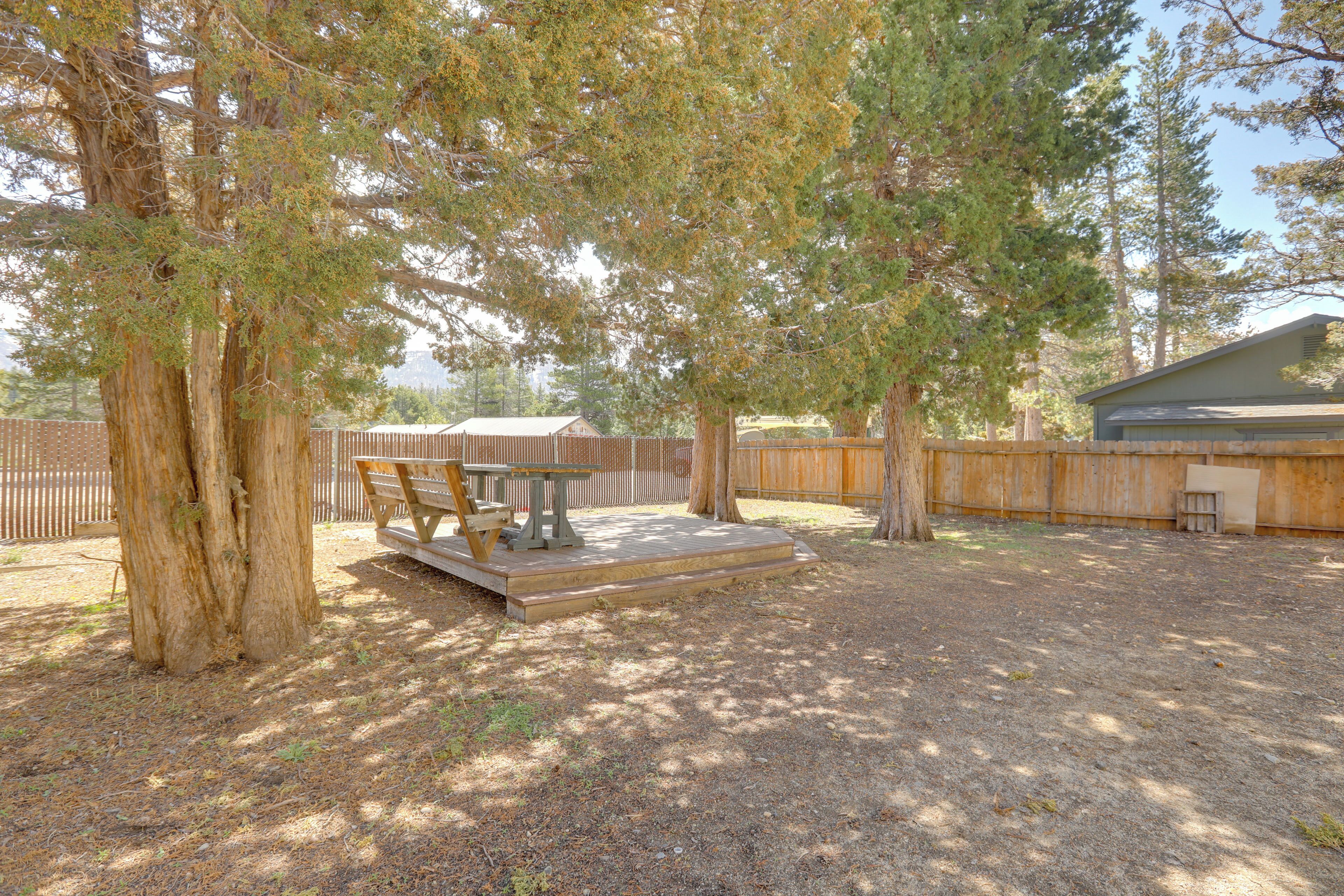 A backyard with a wooden deck, a picnic table, and a covered barbecue area.