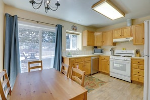 A kitchen with wooden cabinets, a stove, a microwave, and a dining area with a table and chairs. - 9 Mi to Heavenly Mountain: South Lake Tahoe Home (South Lake Tahoe)