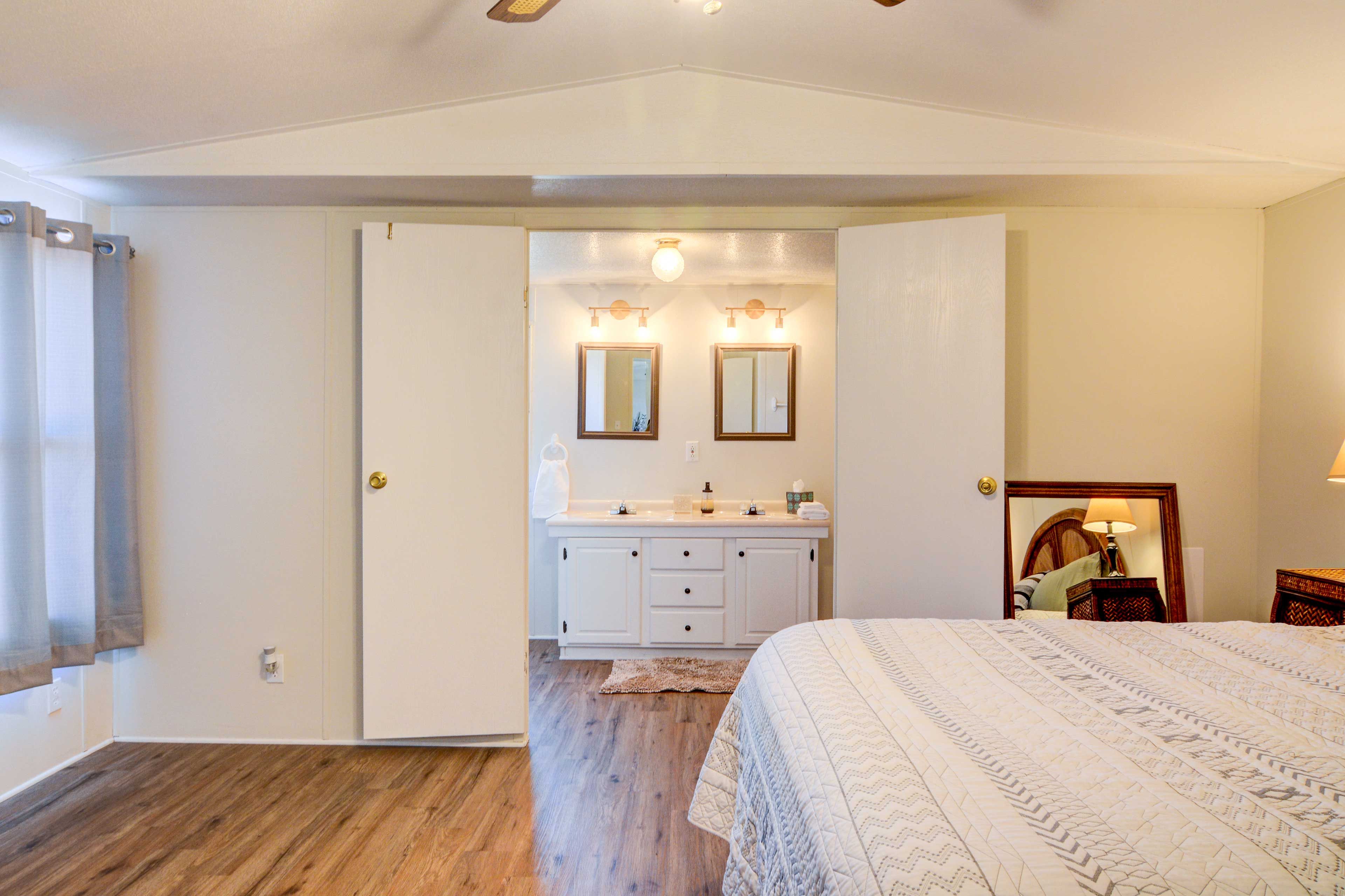 A bedroom with a bed, a dresser with a mirror, and a bathroom with a sink and mirror.