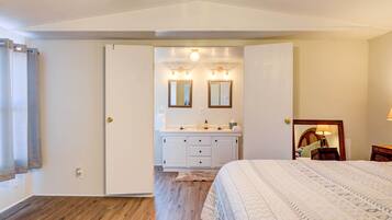 A bedroom with a bed, a dresser with a mirror, and a bathroom with a sink and mirror.