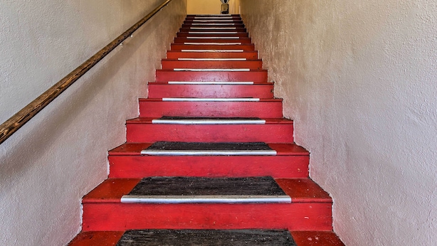 A staircase with alternating red and black steps, a wooden handrail, and a potted plant at the top. - Oregon Getaway by Willamette National Forest! (Oakridge)