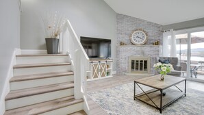A modern living room with a staircase, a fireplace, and a television.