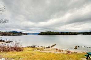 A lakeside view with a picnic table, calm water, and distant hills. - Newfound Lake Vacation Rental w/ Deck & Lake View (Bristol)