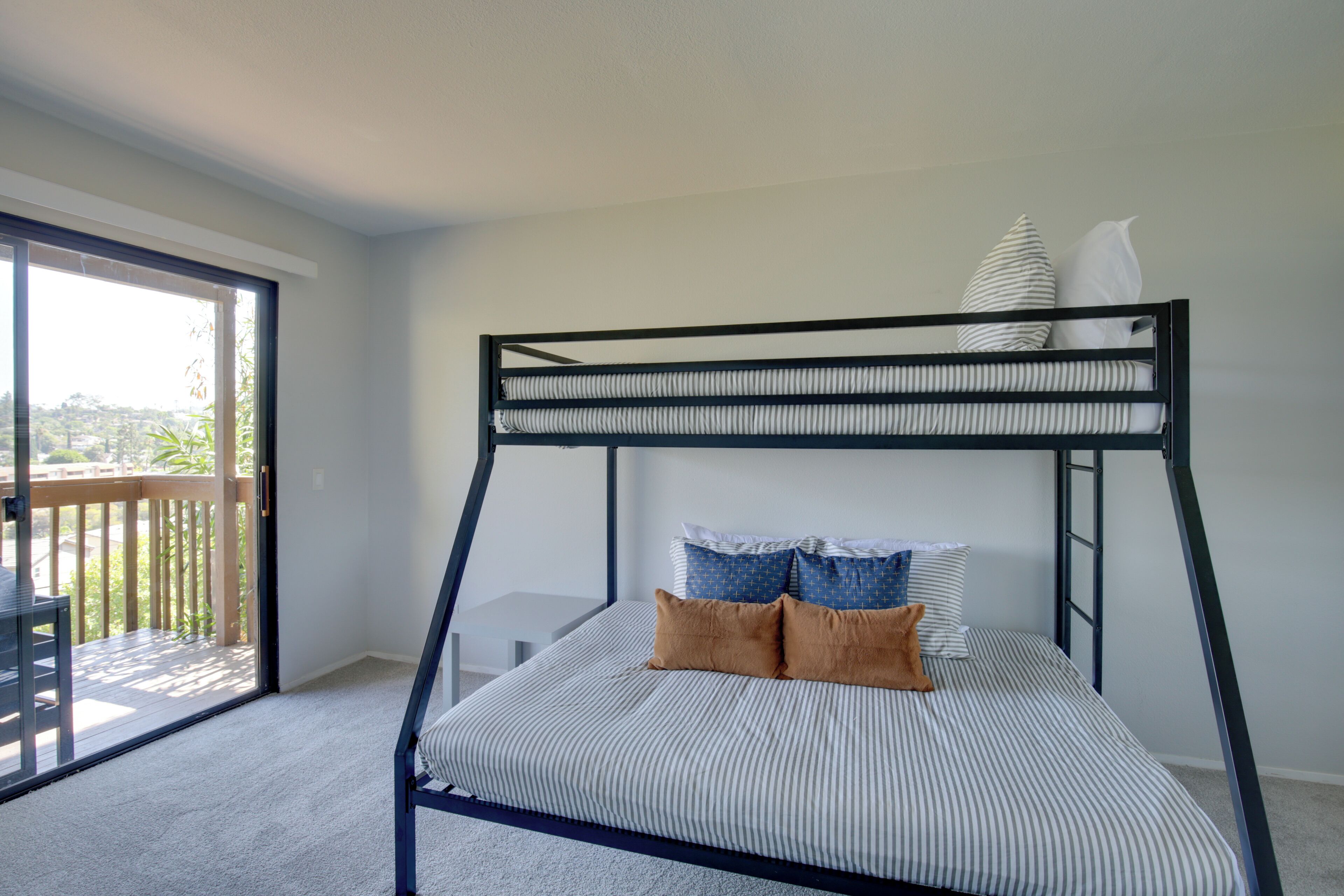 Una cama litera con ropa de cama a rayas y dos almohadas, una terraza de madera y una puerta corrediza al balcón.